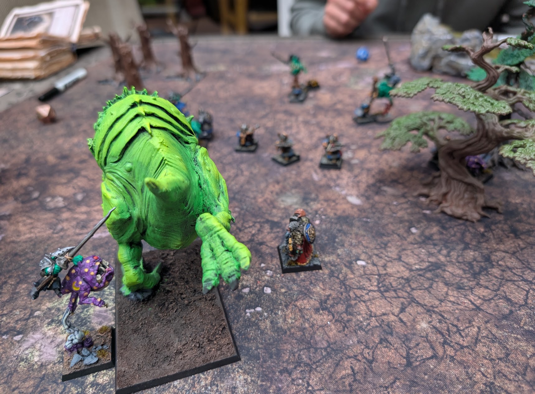 Rear view of the Colossal Squig towering over nearby dwarf and goblin miniatures on rocky ground.